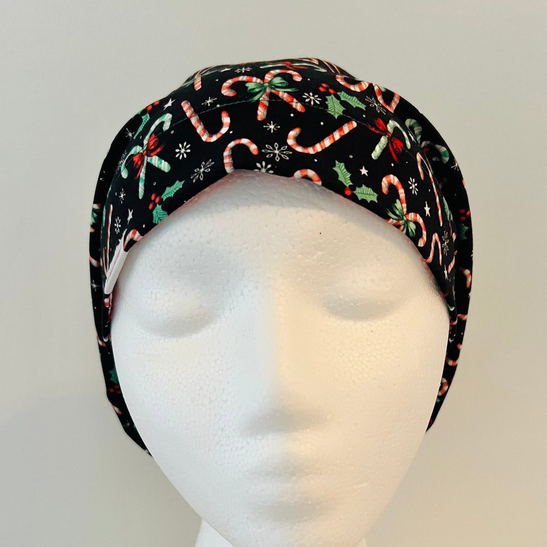 Christmas Candy Cane Euro scrub cap with festive candy canes, holly leaves, bows, stars, and snowflakes on a black background, comfortable surgical cap for nurses, surgeons, doctors, and healthcare professionals, front view.