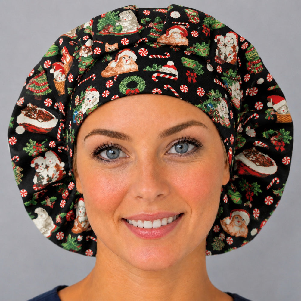 Woman wearing a Christmas cat bouffant scrub cap, front view — festive kittens in Santa hats with candy canes and peppermints on black, adjustable women's surgical hat