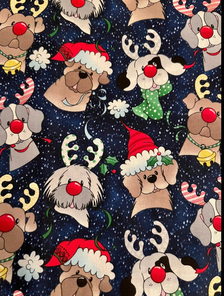 Fabric detail of the Christmas dog scrub cap — close-up of red-nosed reindeer puppies and jingle bells on snowy navy cotton