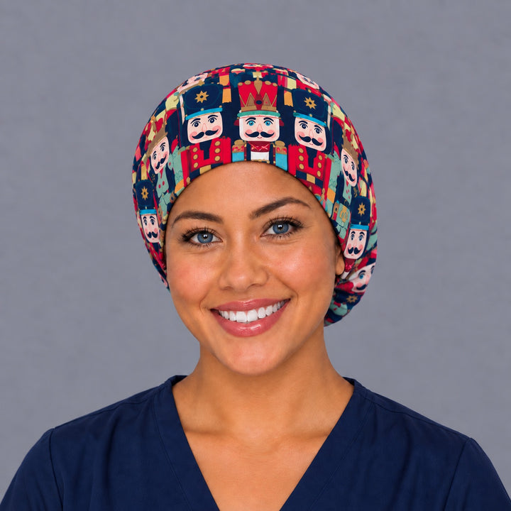 Woman wearing a Christmas nutcracker Euro scrub cap, front view — red and teal nutcracker soldiers on navy, adjustable holiday surgical hat