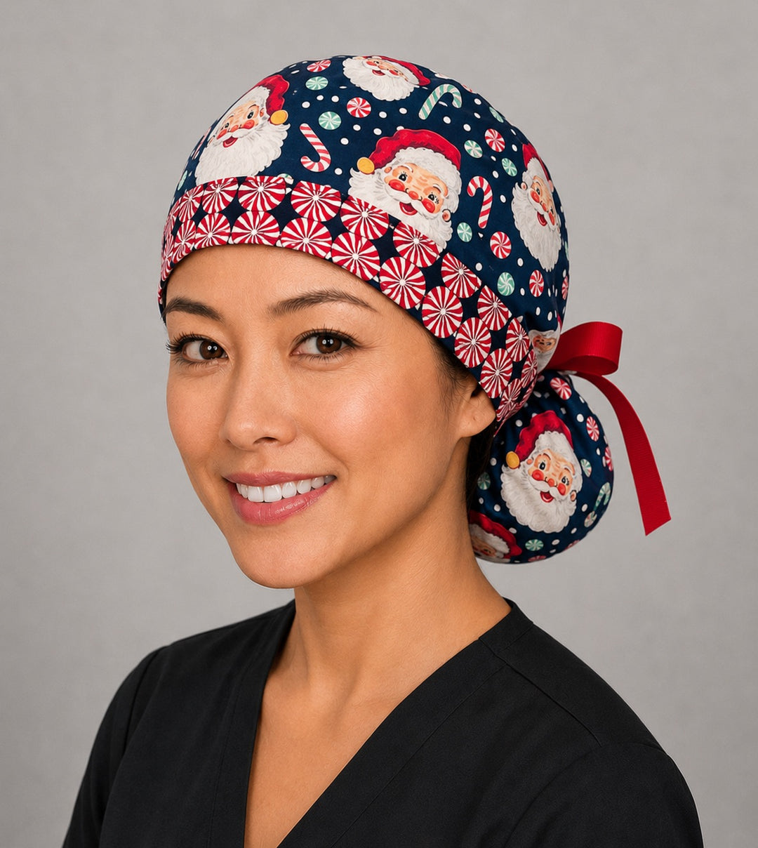 Woman wearing Christmas Santa ponytail scrub cap, front view smiling with vintage Santa faces, peppermints and candy canes on navy with peppermint band and red ribbon tie