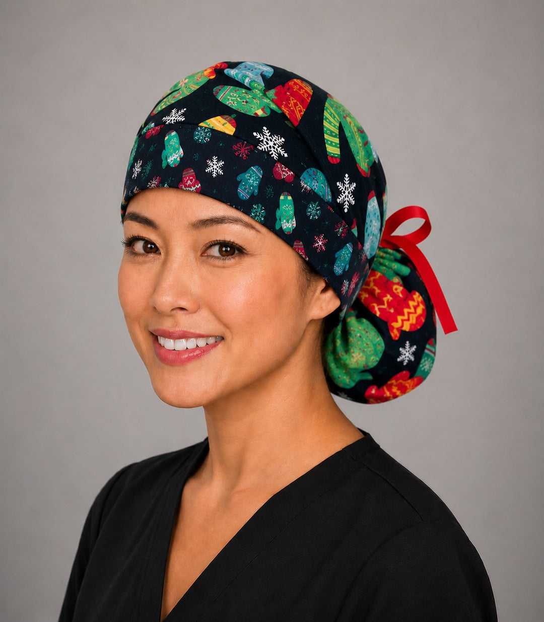Christmas ugly sweater ponytail surgical cap right three-quarter angle showing knit sweaters, mittens and snowflakes on black with red ribbon bow