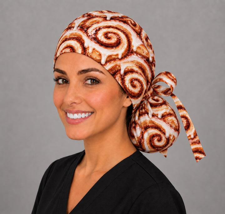 Surgical nurse wearing a funny cinnamon roll ponytail scrub cap with glazed cinnamon buns and a ribbon tie, an OR World original food print surgical hat for long hair