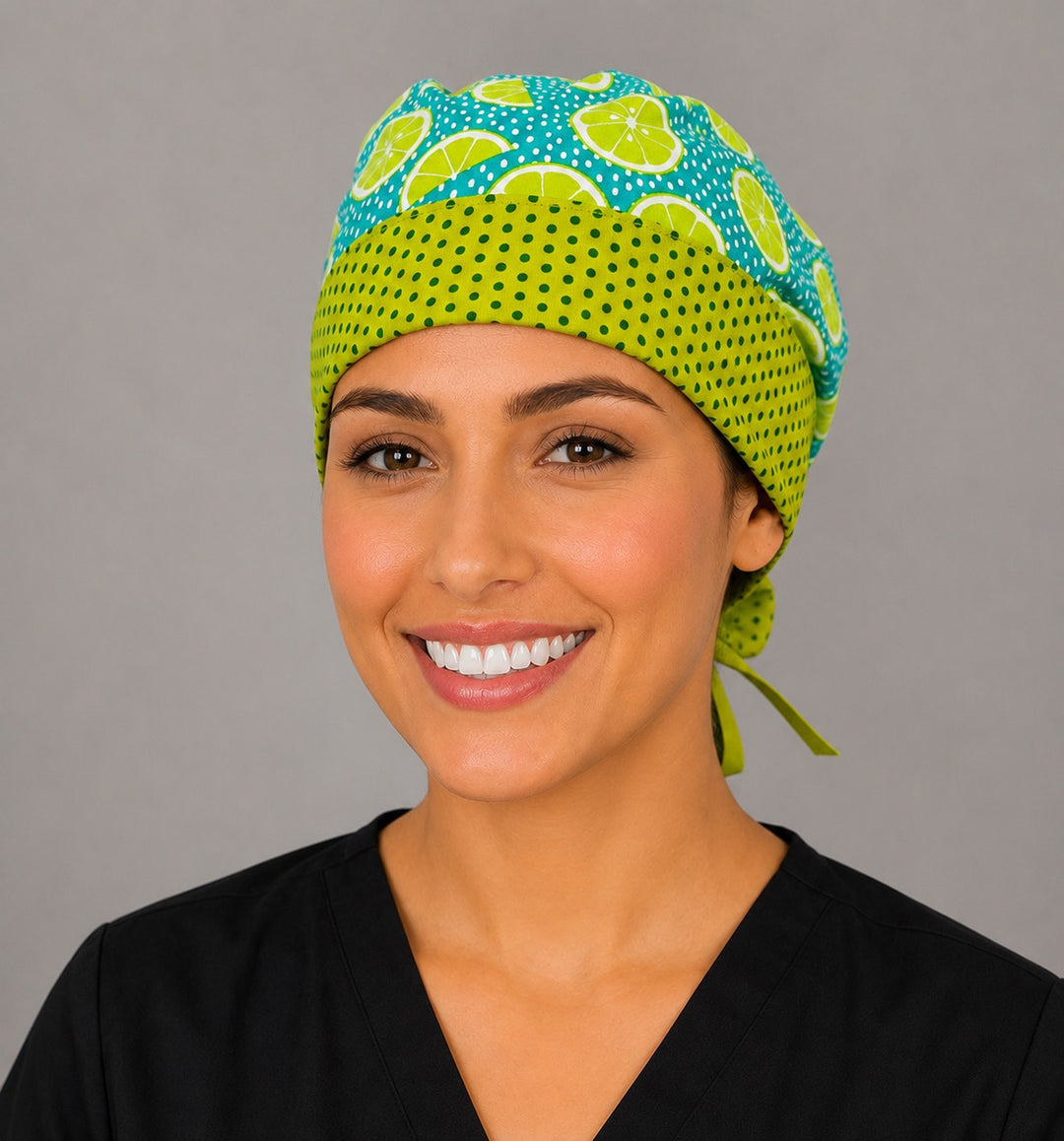Woman wearing citrus lemon lime ponytail scrub cap, front view smiling with lime slices on teal, lime green polka dot band and green ribbon tie