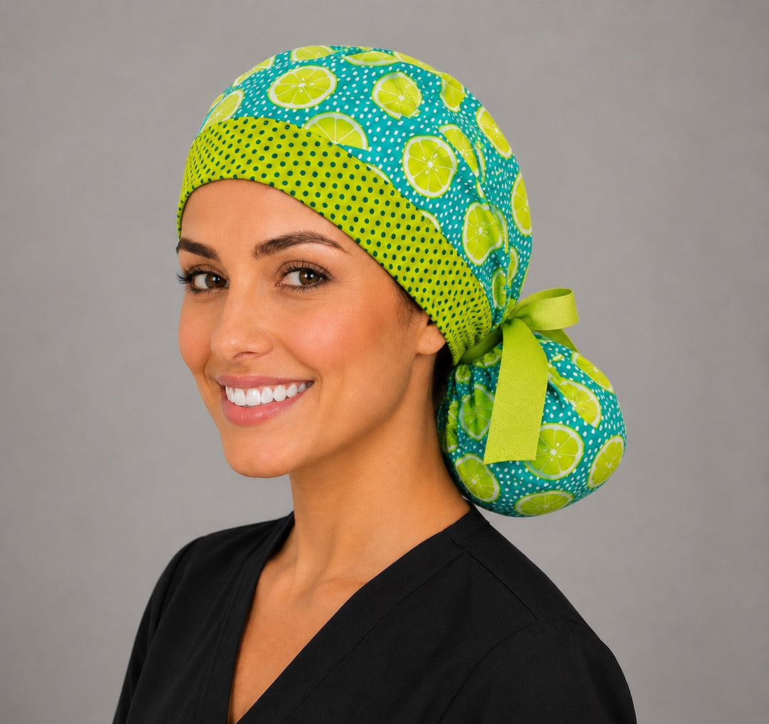 Citrus lemon lime ponytail nurse cap right three-quarter angle on smiling model showing lime and lemon slices, teal ground and green ribbon bow