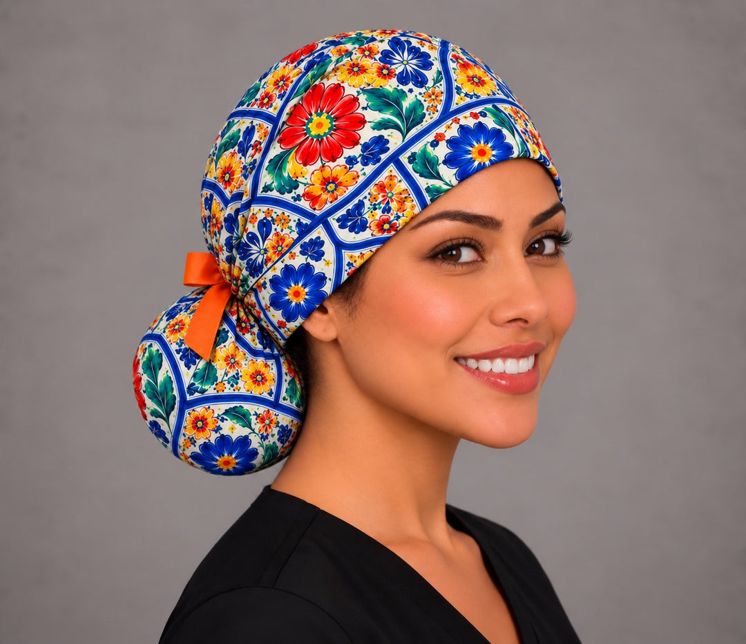 Right three-quarter angle of a cobalt blue tile print scrub cap for long hair, with a large red bloom on the crown and the ponytail pouch holding hair low