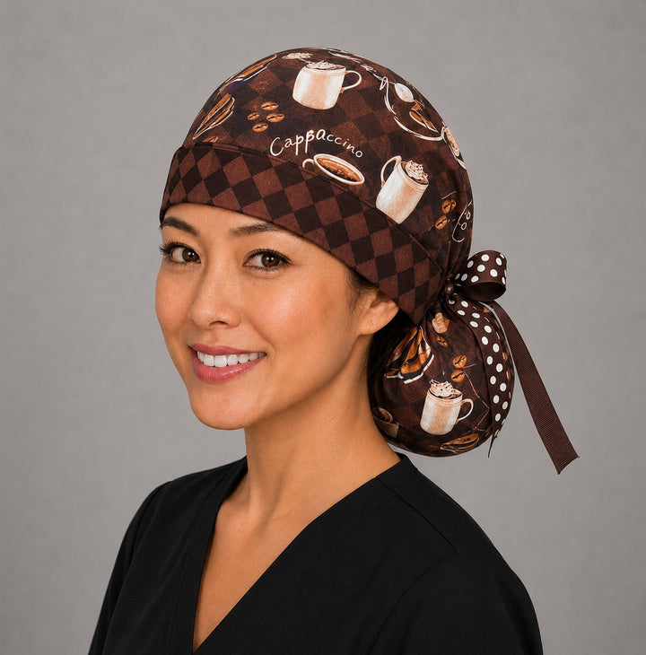 Woman wearing brown coffee lover ponytail scrub cap, front view smiling with cappuccinos, lattes and coffee beans on brown checkerboard with polka dot ribbon tie