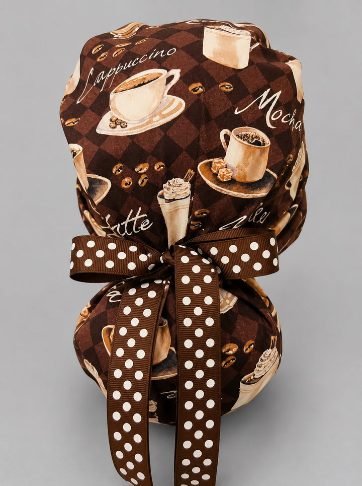 Brown coffee lover ponytail nurse cap right three-quarter angle on smiling model showing cappuccino, mocha and coffee bean print with brown polka dot ribbon bow