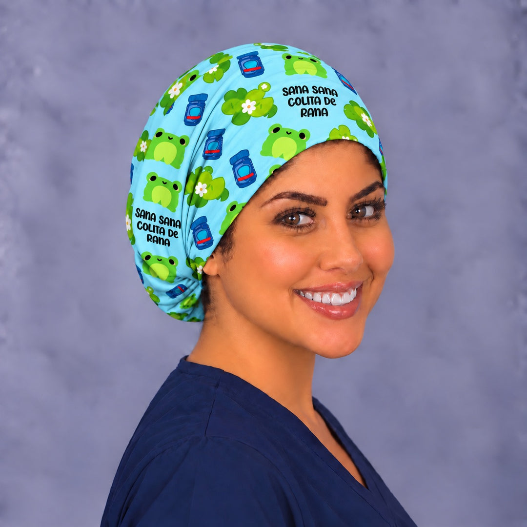 Three-quarter angle of a Colita de Rana surgical cap, with smiling green frogs and lily pads with white flowers wrapping the side band