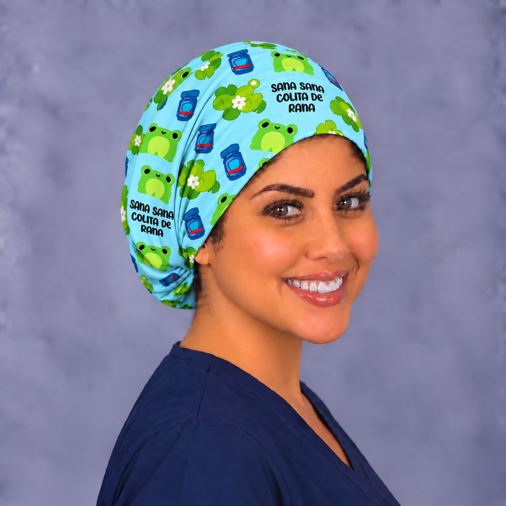 Three-quarter angle of a Colita de Rana surgical cap, with smiling green frogs and lily pads with white flowers wrapping the side band