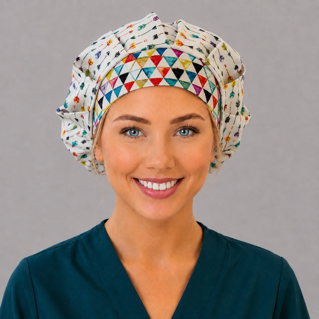 Woman wearing a colorful arrows bouffant scrub cap, front view — watercolor arrows on white with a rainbow triangle band, adjustable women&