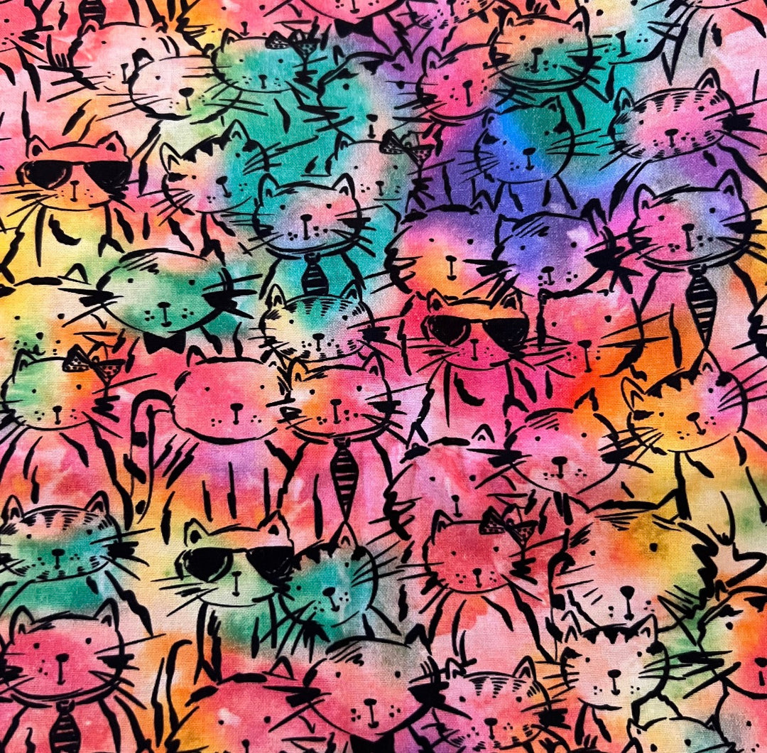 Fabric detail of the colorful cats scrub cap — close-up of hand-drawn kitty faces on rainbow tie-dye cotton