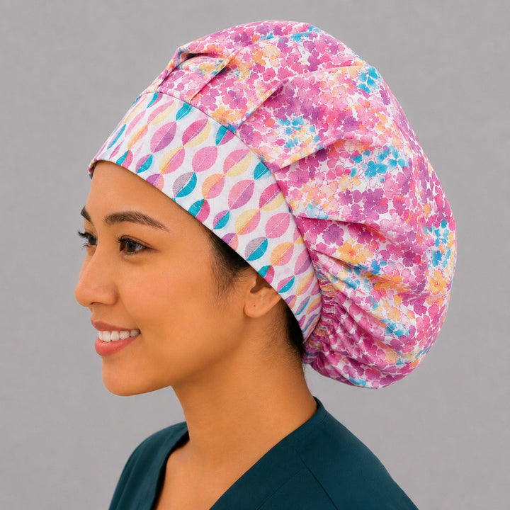 Colorful floral watercolor bouffant scrub cap left three-quarter angle on smiling model showing bright pink teal orange watercolor florals with geometric band, women&