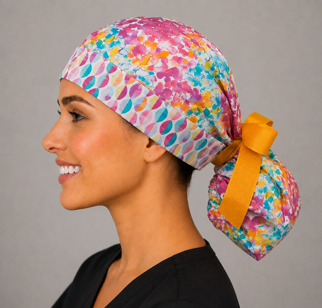 Colorful floral watercolor ponytail scrub cap back view close-up showing gathered pouch full of pink teal orange watercolor florals and gold ribbon bow