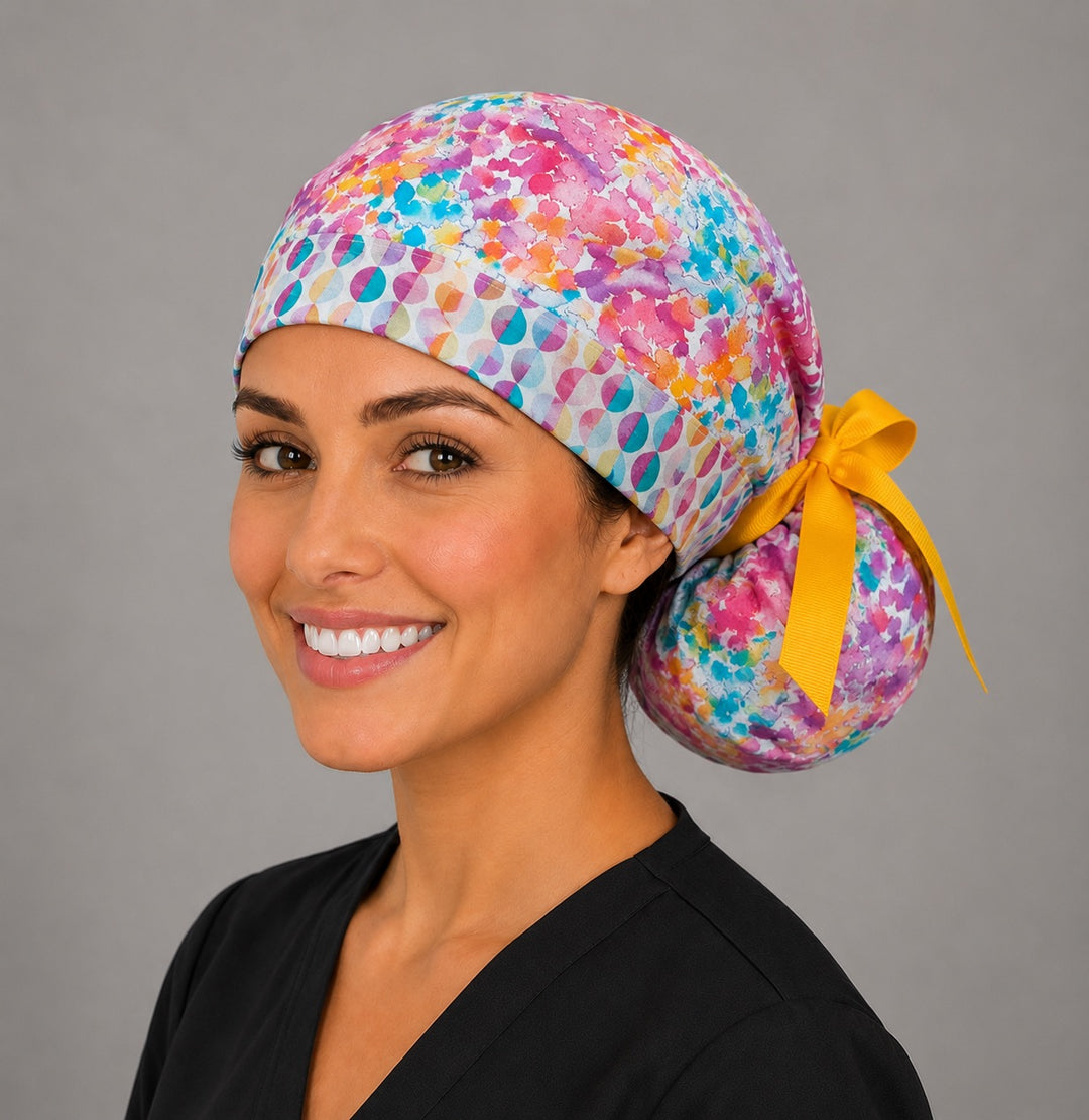 Colorful floral watercolor ponytail surgical cap left three-quarter angle showing gathered ponytail pouch of pink teal orange watercolor print and gold grosgrain ribbon bow