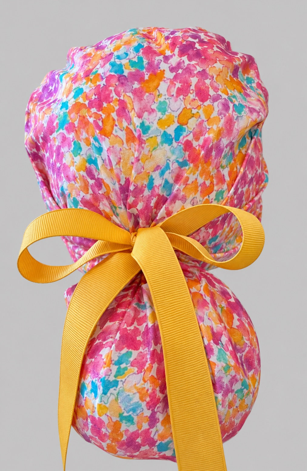 Colorful floral watercolor ponytail scrub cap right side profile showing gathered pouch of pink teal orange watercolor florals with geometric band and gold ribbon
