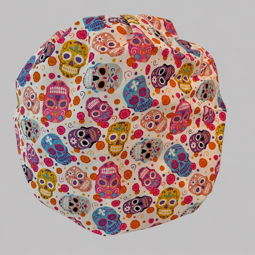 Colorful sugar skull scrub cap fabric close-up showing bright Day of the Dead skulls, marigolds and swirls on cream cotton, OR World Mexico collection
