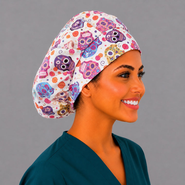 Colorful sugar skull bouffant surgical cap right three-quarter angle on smiling model showing bright Day of the Dead skulls on cream, OR World Mexico collection nurse hat