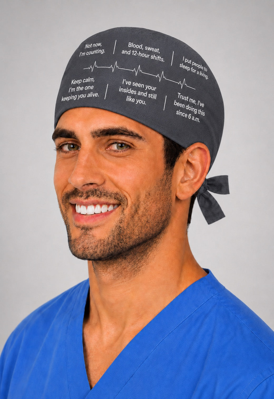 Custom quote scrub cap in charcoal gray with funny medical sayings and heartbeat line, three quarter side view on a male surgeon in blue scrubs, personalized your own words custom text surgical hat, handmade in USA gift for surgeons and OR teams, OR World