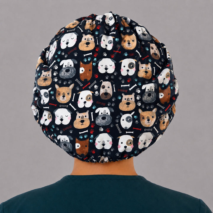 Back view of the cute dog bouffant scrub cap — full roomy fit showing navy puppy faces, bones and paw prints with elastic gather