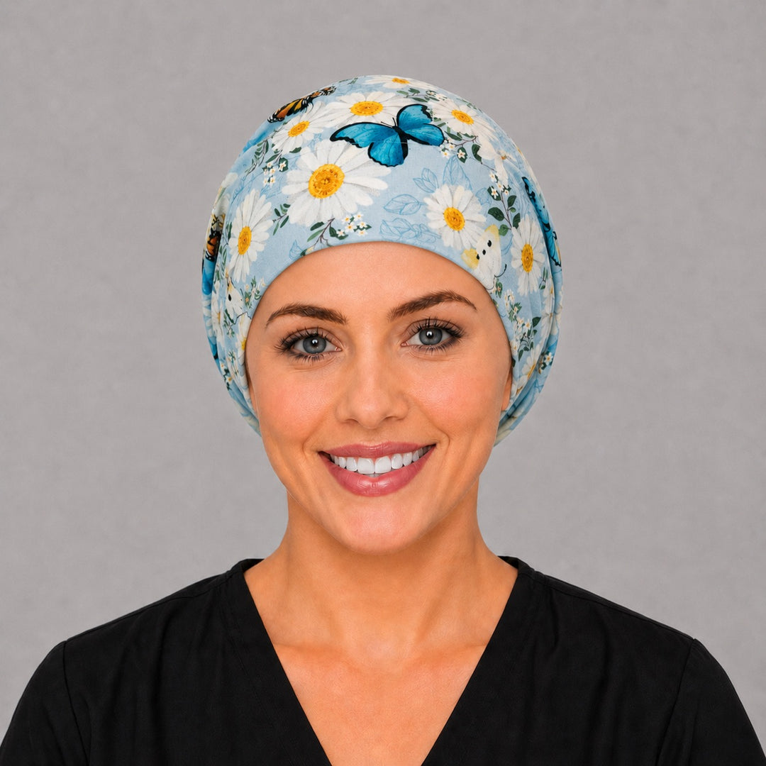 Woman wearing a daisy and butterfly Euro scrub cap, front view — white daisies and monarchs on sky blue, adjustable fitted surgical hat for women