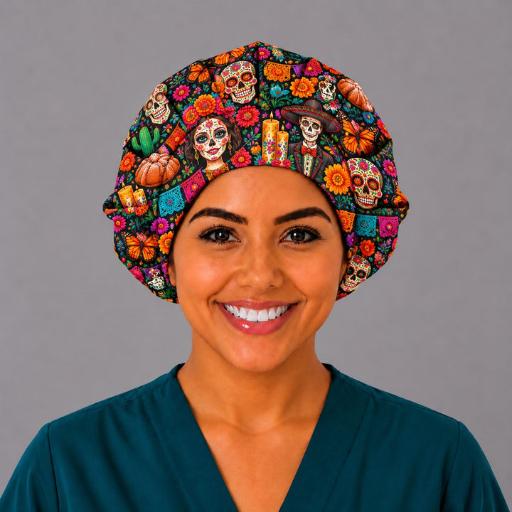 Front view of a Day of the Dead bouffant scrub cap for long hair with colorful calaveras, candles and cempasúchil marigolds on black, worn by a smiling nurse in teal scrubs