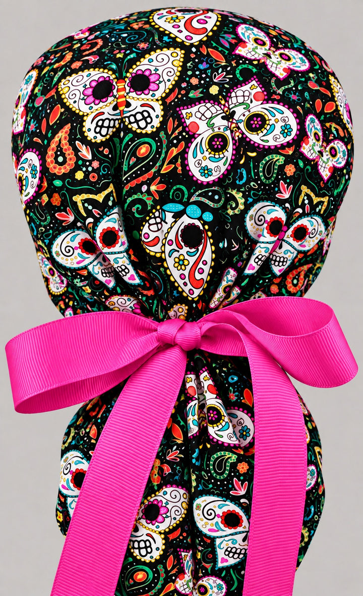 Back of the Día de los Muertos ponytail cap, pink grosgrain ribbon tied in a bow above the gathered hair pouch, gorro quirúrgico mexicano