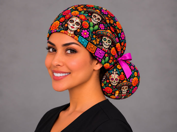 Smiling Latina nurse in a Día de Muertos ponytail scrub cap with a fuchsia bow, catrina and papel picado, left angle view of the OR World original print