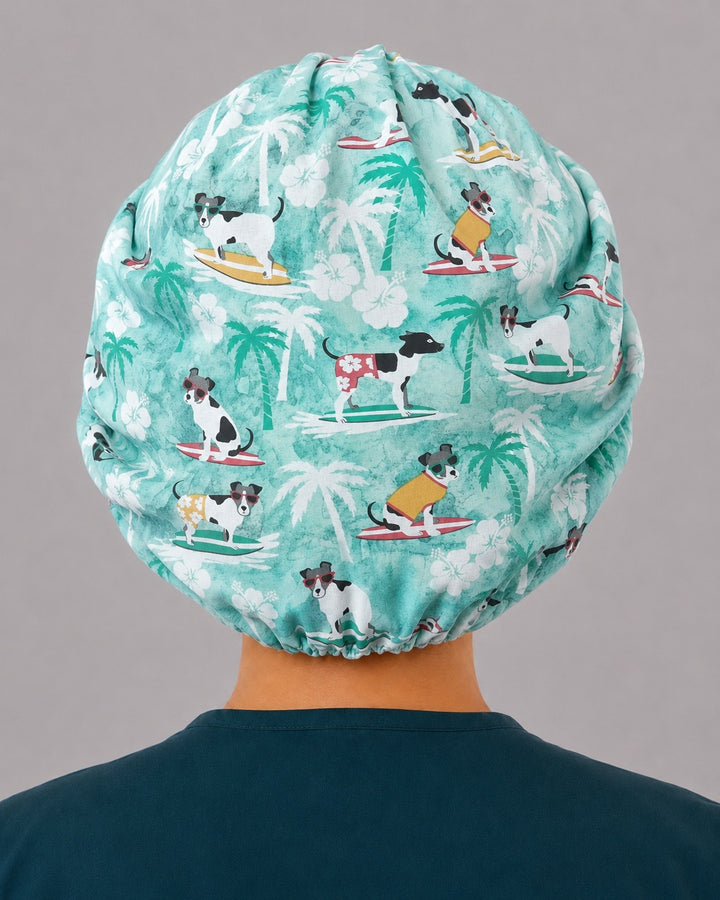 Back view of the dog surfers bouffant scrub cap — full roomy fit showing surfing dogs and palm trees, complete hair coverage with elastic gather