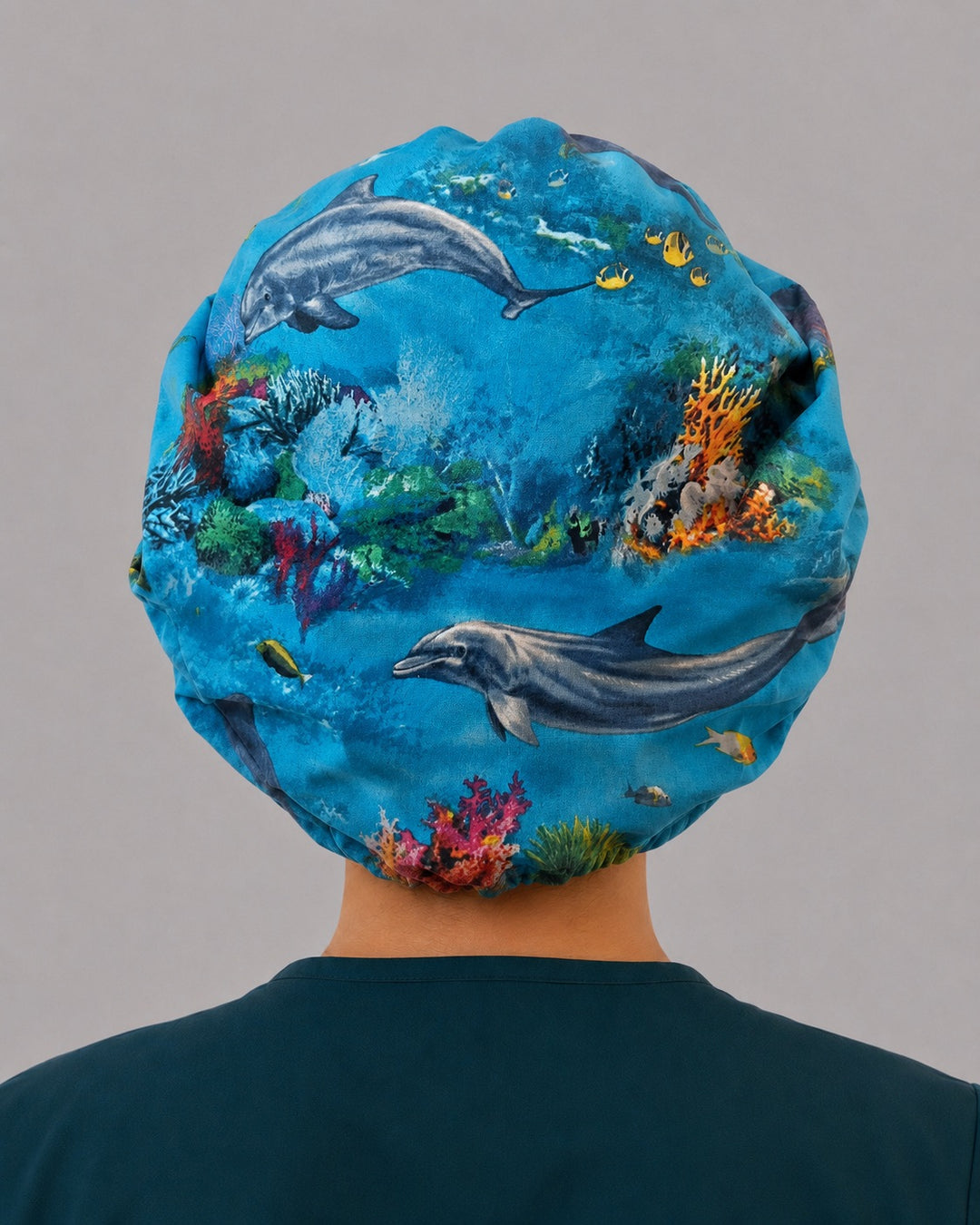 Back view of the dolphin bouffant scrub cap — full roomy fit showing two dolphins swimming over a colorful coral reef