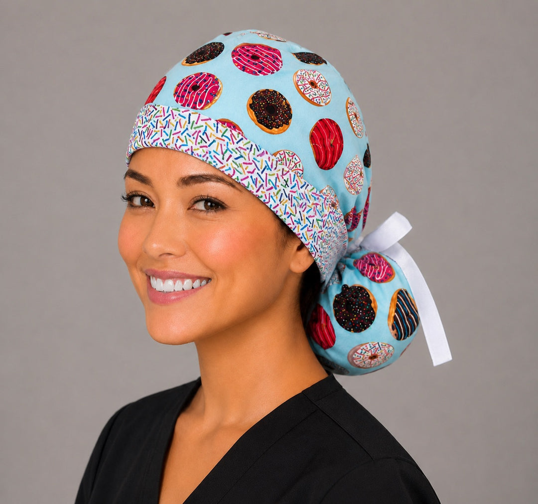 Left three-quarter angle of donut print ponytail scrub cap for women showing colorful frosted donuts, sprinkle headband and white ribbon bow
