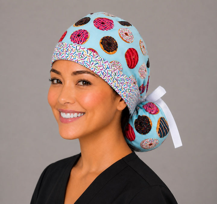 Left three-quarter angle of donut print ponytail scrub cap for women showing colorful frosted donuts, sprinkle headband and white ribbon bow