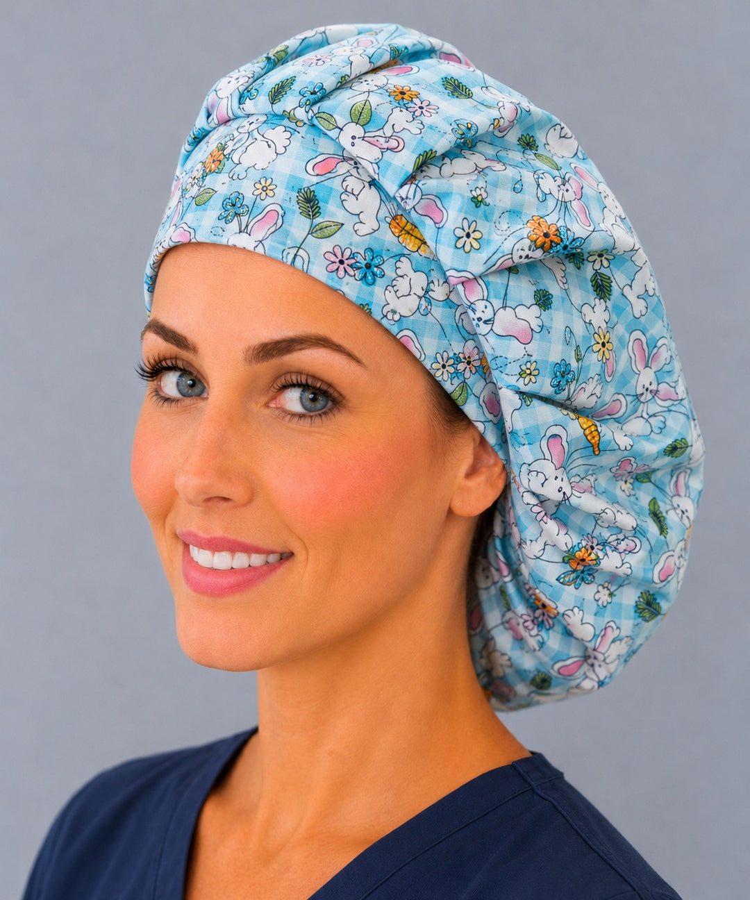 Woman wearing an Easter bunny bouffant scrub cap — white rabbits with carrots and spring flowers on aqua gingham, adjustable women's surgical hat