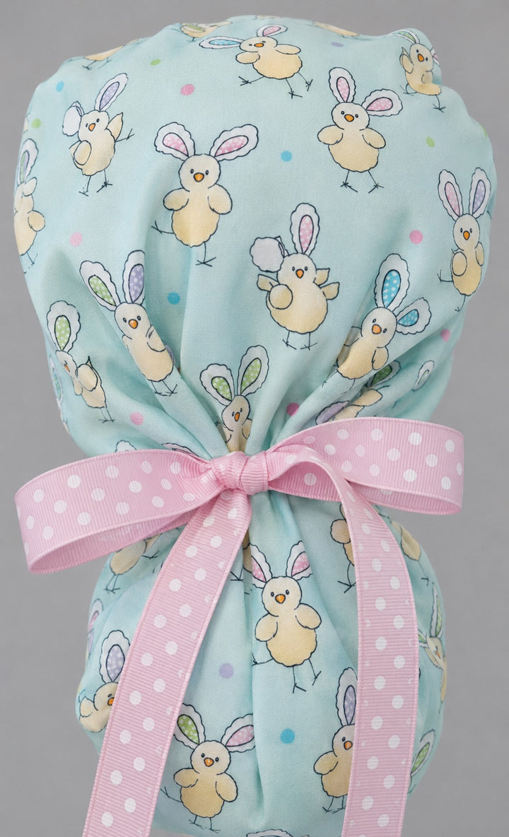 Easter chickens ponytail scrub cap back view close-up showing gathered pouch full of bunny-ear chicks and colorful dots on aqua with pink polka-dot ribbon bow
