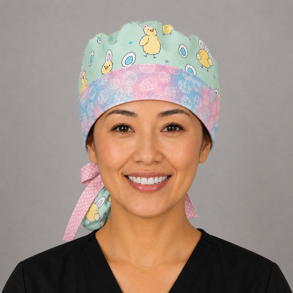 Woman wearing Easter chickens ponytail scrub cap, front view smiling with bunny-ear chicks and Easter eggs on aqua with pastel egg band and pink polka-dot ribbon tie