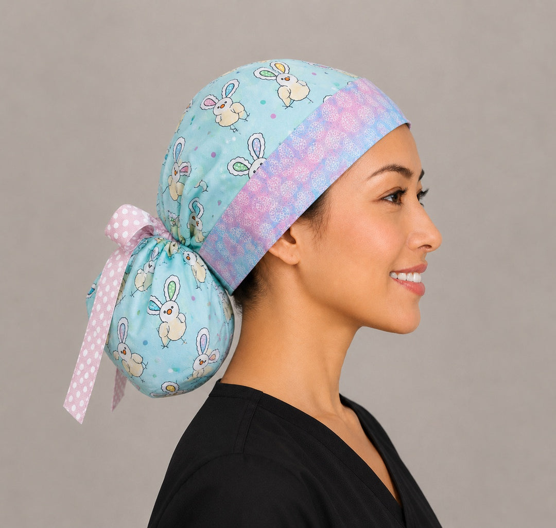 Easter chickens ponytail scrub cap right three-quarter angle on smiling model showing bunny-ear chicks, Easter eggs and pastel egg band with pink polka-dot ribbon bow