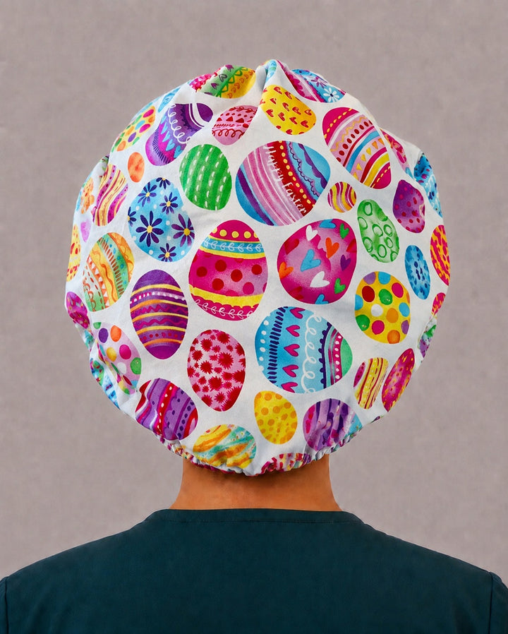 Back view of the Easter egg bouffant scrub cap — full gathered fit showing decorated eggs in pink, turquoise, purple and yellow on white