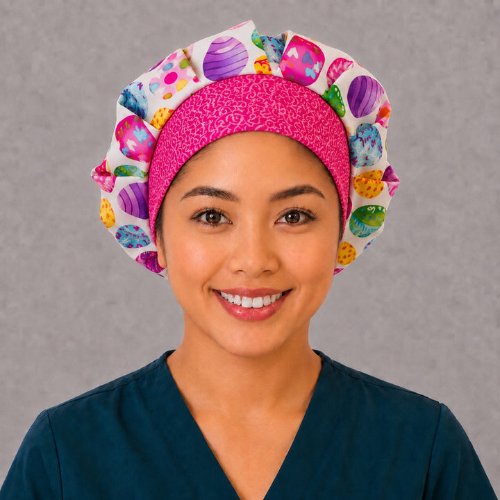 Woman wearing an Easter egg bouffant scrub cap, front view — colorful decorated eggs on white with a hot-pink swirl band, adjustable women&