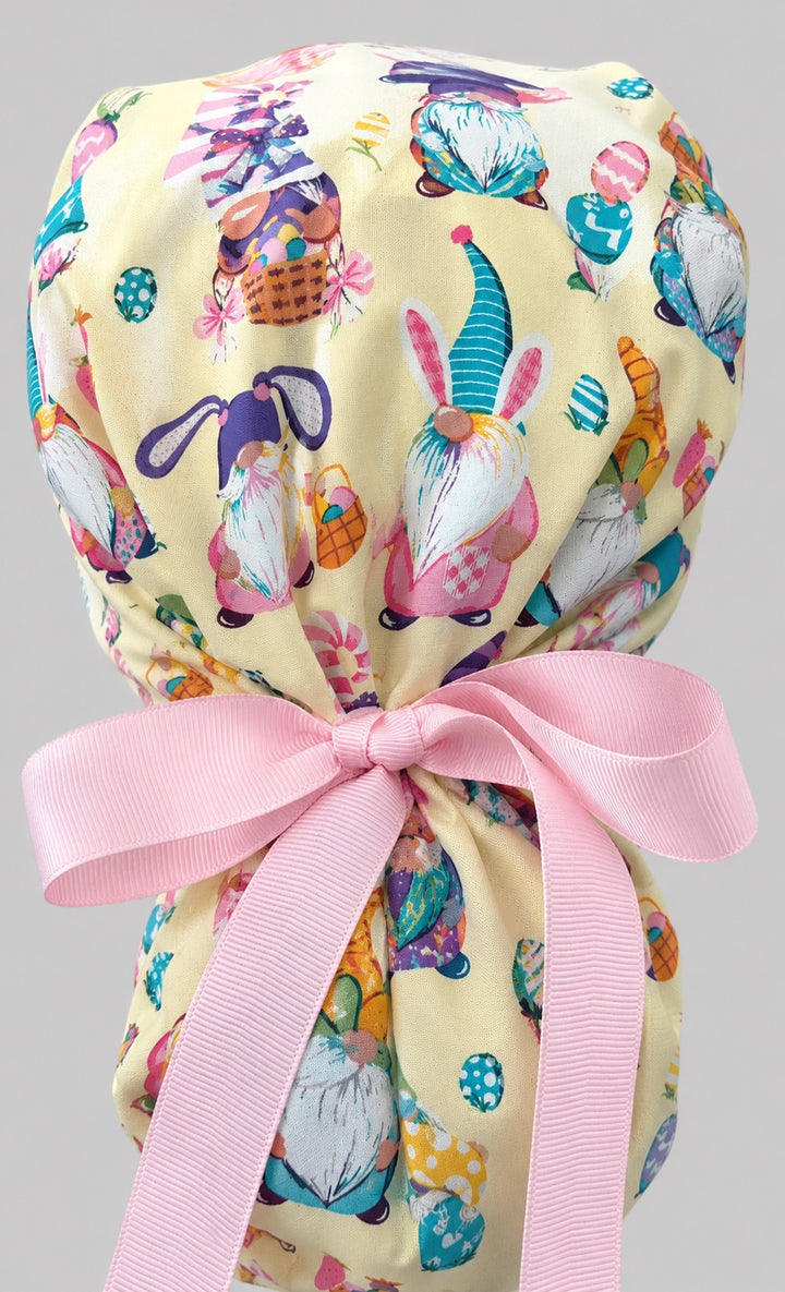 Easter gnomes ponytail scrub cap back view close-up showing gathered pouch full of pastel gnomes in bunny ears, Easter eggs and baskets with pink grosgrain ribbon bow