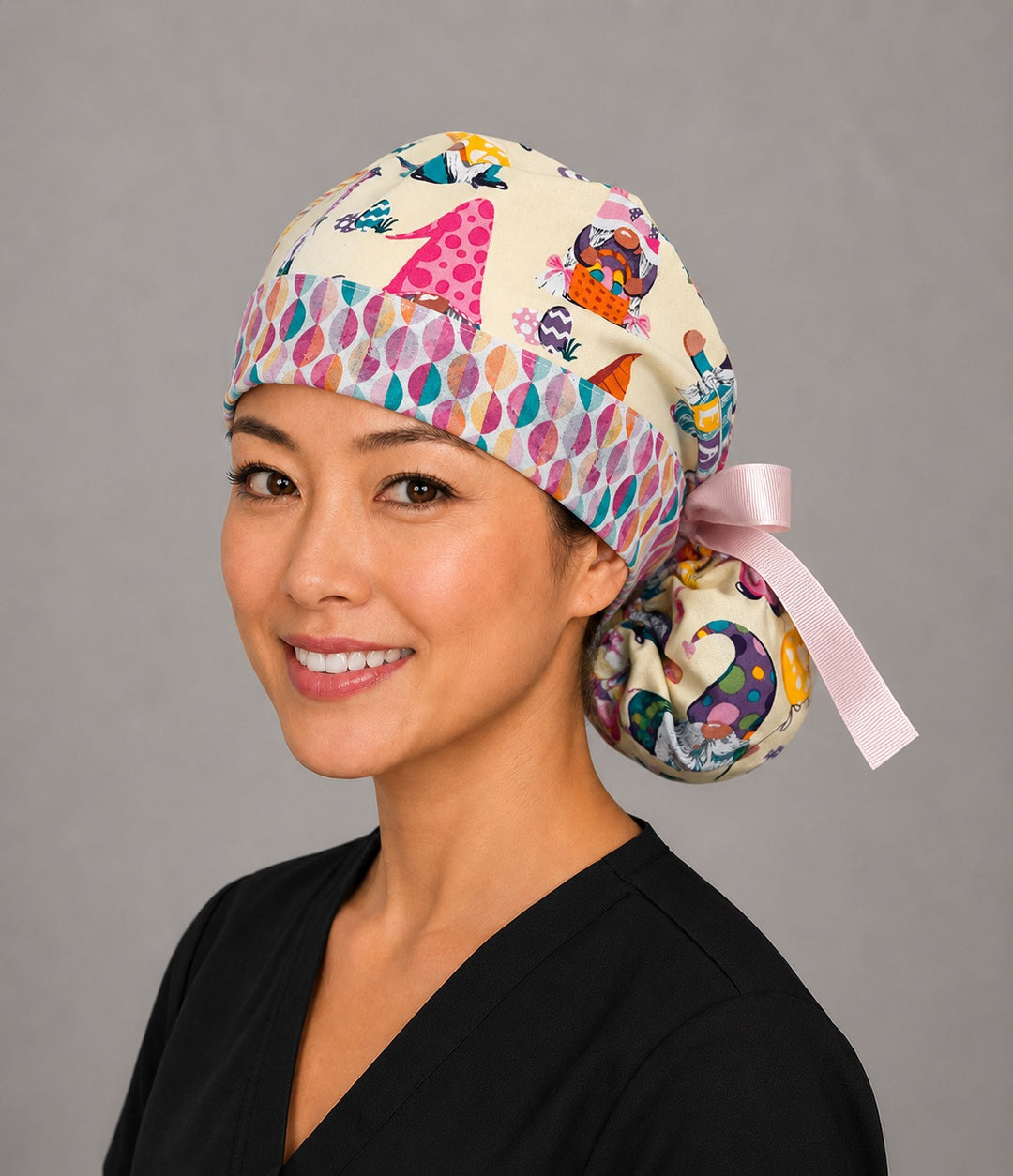 Easter gnomes ponytail nurse cap left three-quarter angle on smiling model showing pastel gnomes, Easter eggs and egg band with pink ribbon bow