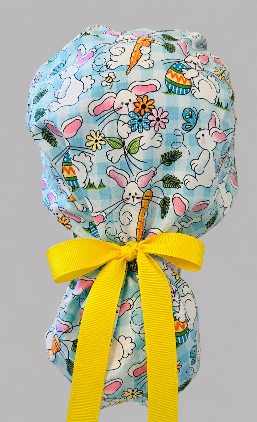 Easter rabbits and carrots ponytail scrub cap back view close-up showing gathered pouch full of bunnies, Easter eggs, flowers and butterflies on aqua gingham with yellow ribbon bow