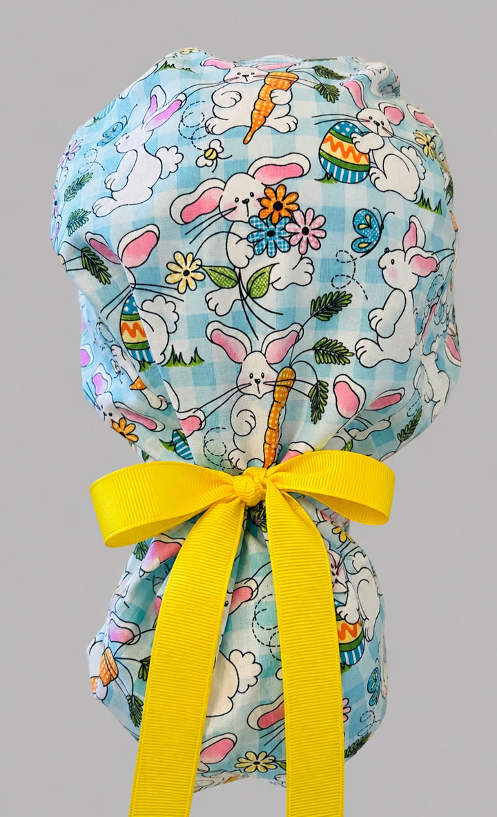 Easter rabbits and carrots ponytail scrub cap back view close-up showing gathered pouch full of bunnies, Easter eggs, flowers and butterflies on aqua gingham with yellow ribbon bow