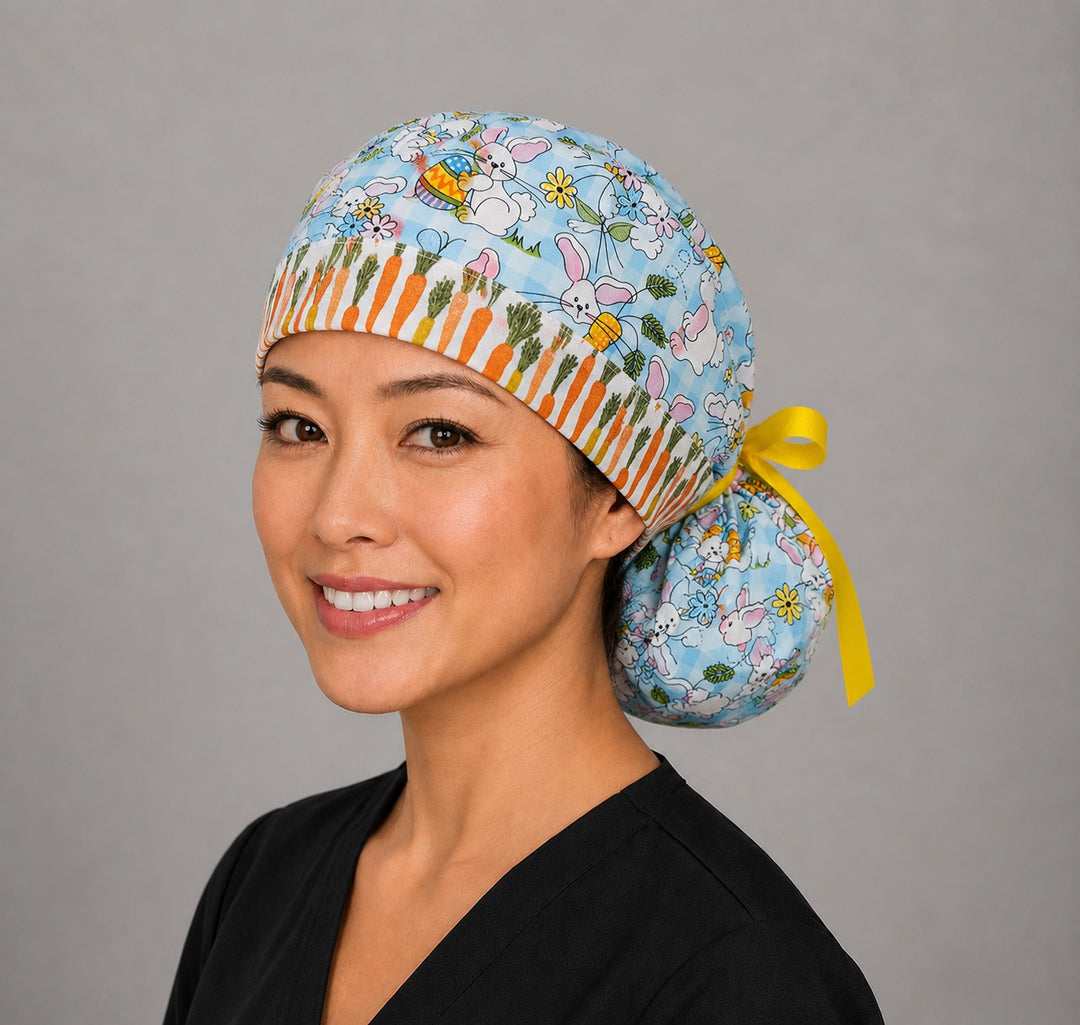 Woman wearing Easter rabbits and carrots ponytail scrub cap, front view smiling with bunnies, eggs and flowers on aqua gingham with carrot band and yellow ribbon tie