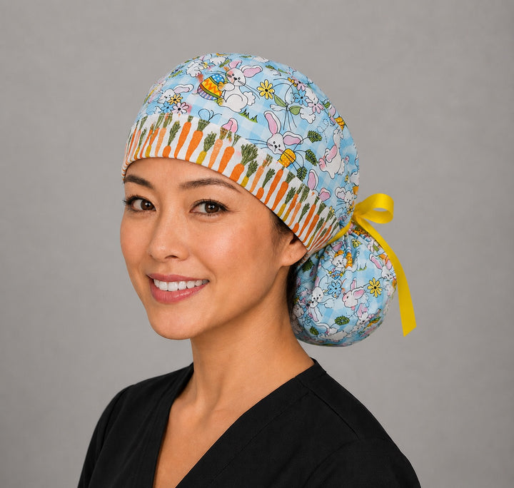 Woman wearing Easter rabbits and carrots ponytail scrub cap, front view smiling with bunnies, eggs and flowers on aqua gingham with carrot band and yellow ribbon tie