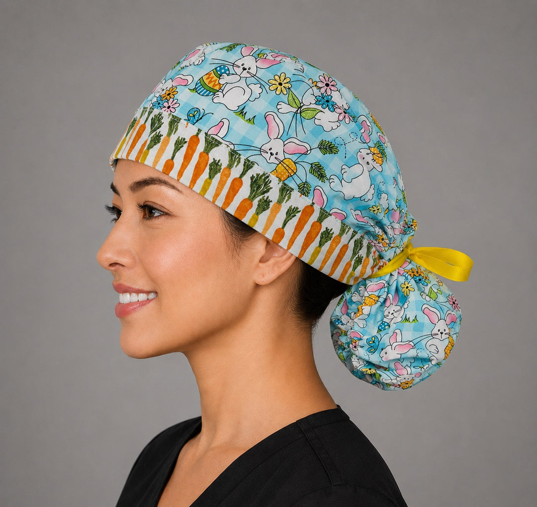 Easter rabbits and carrots ponytail scrub cap left three-quarter angle showing bunnies, eggs, carrots and carrot band with yellow ribbon bow
