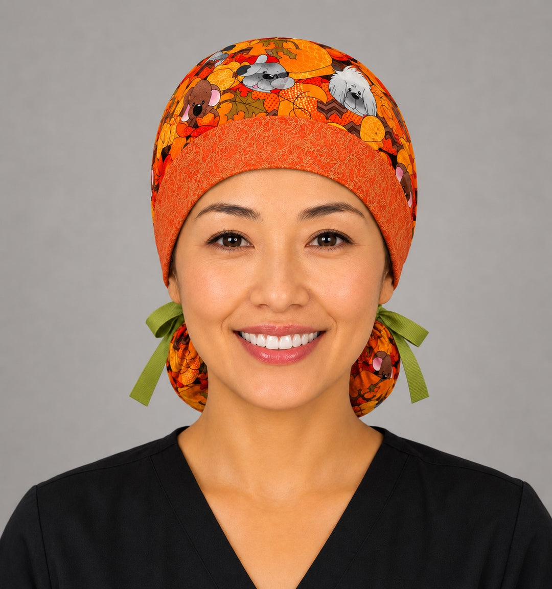 Fall dog ponytail scrub cap front view on smiling model showing puppies among pumpkins and autumn leaves with orange contrast band and green ribbon ties