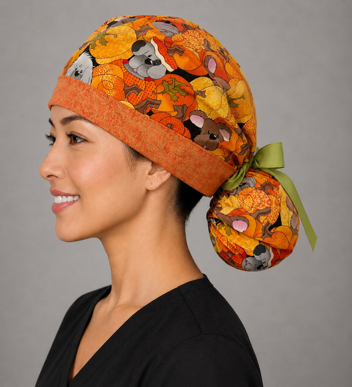 Fall dog ponytail surgical cap left side profile showing gathered ponytail pouch of pumpkin puppies and autumn leaves with orange band and green ribbon bow