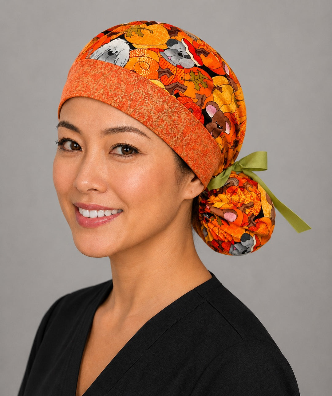 Fall dog ponytail nurse cap left three-quarter angle on smiling model showing pumpkin puppies, autumn leaves and orange band with green ribbon bow