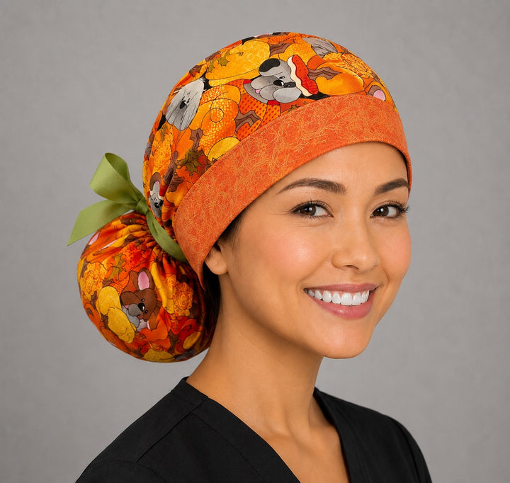 Fall dog ponytail scrub cap right three-quarter angle showing pumpkin puppies and autumn leaves with orange contrast band and green ribbon bow