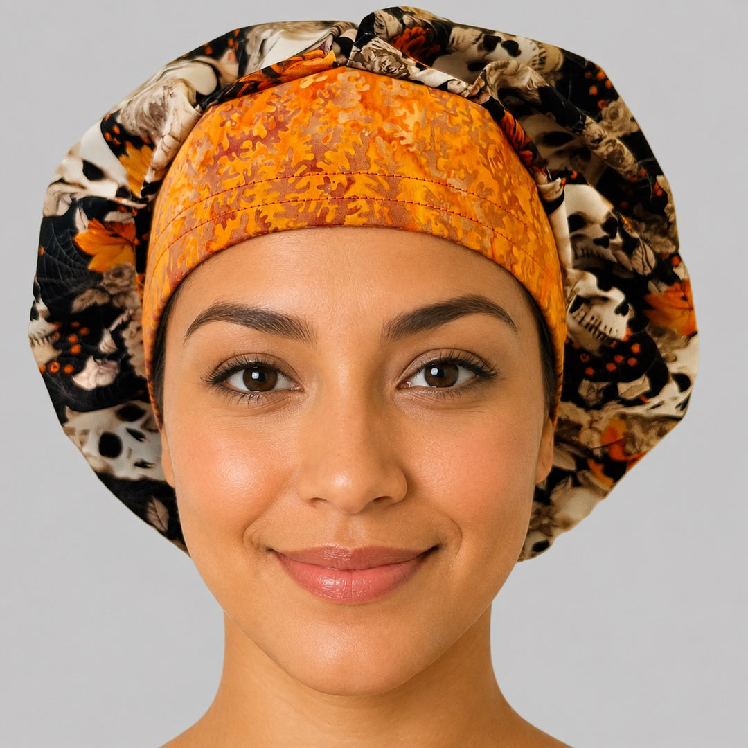 Woman wearing a fall skull bouffant scrub cap, front view — ivory skulls and autumn florals on black with burnt-orange batik band, adjustable women's surgical hat